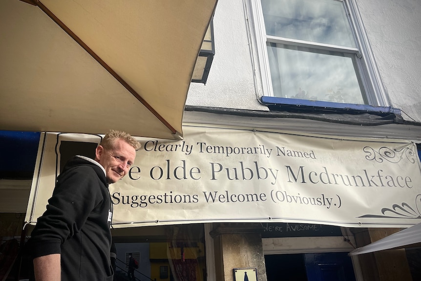 A man next to a a sign reading "Ye Olde Pubby Mcdrunkface" 