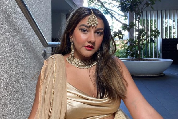 A woman wearing a gold sari and jewelry sitting on the ground 