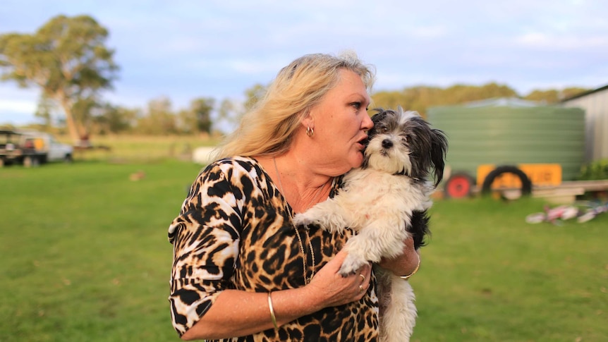 A woman on a rural property hugging a small black and white dog