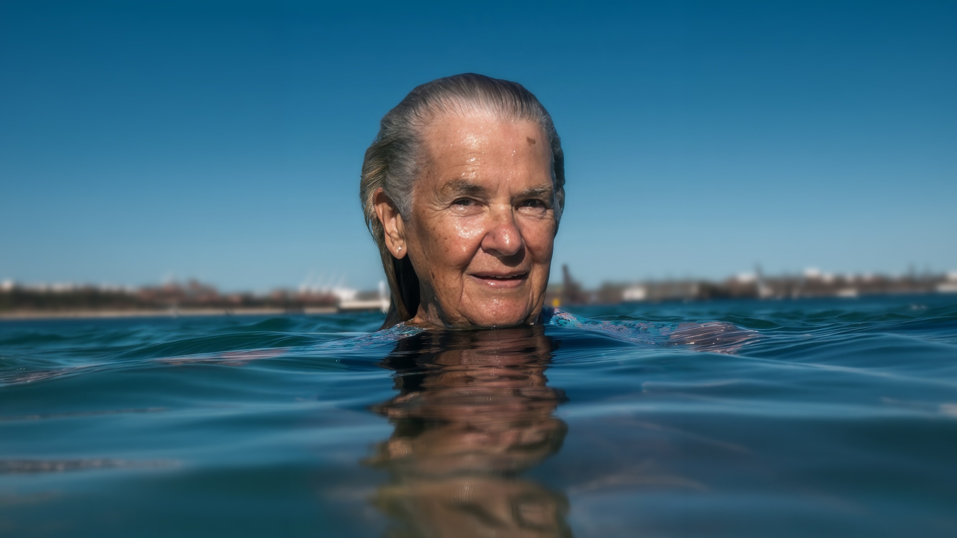 The face of Keitha Bradley smiling as she floats with her head above the ocean water 