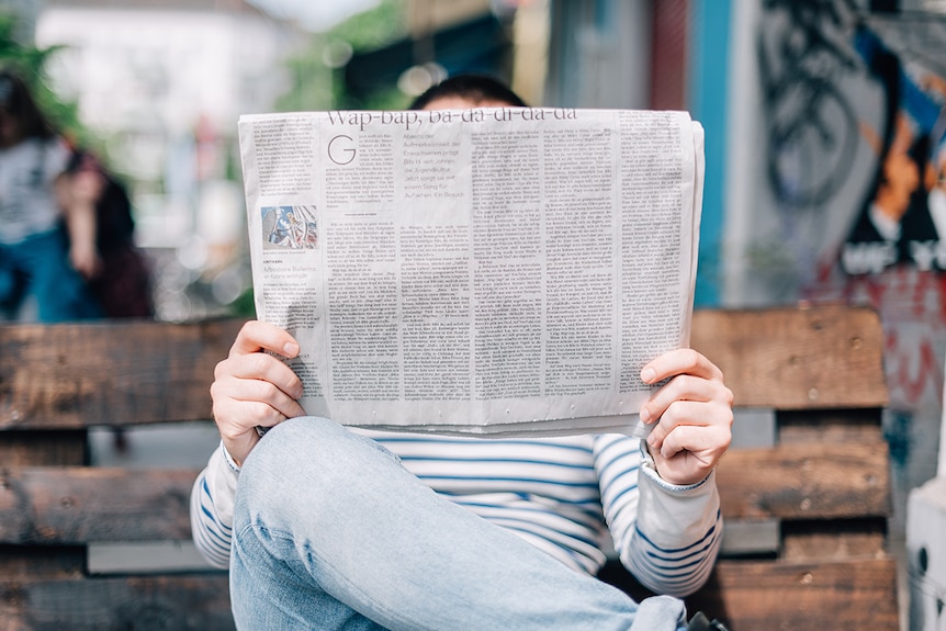 A man reading a newspaper on a park bench.