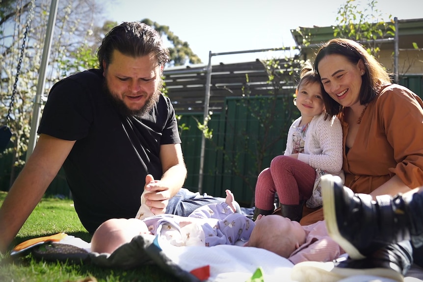 Two parents with their twins and two other young children on a picnic rug