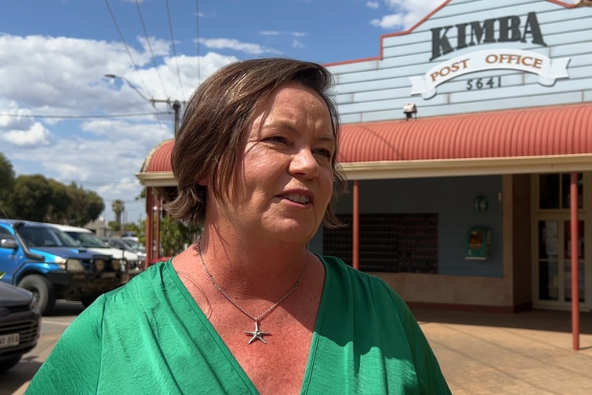 A woman in a green top stands in front of an outback post office