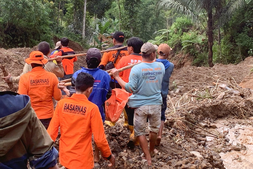 A group of rescue workers wearing orange and carrying bags walking in mud