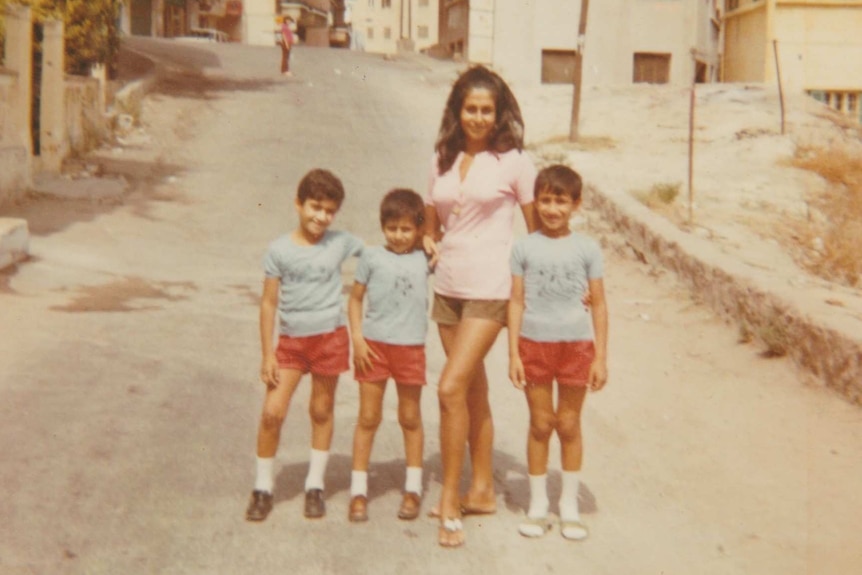 A women and three boys stand in the street all wearing shorts and t-shirts.