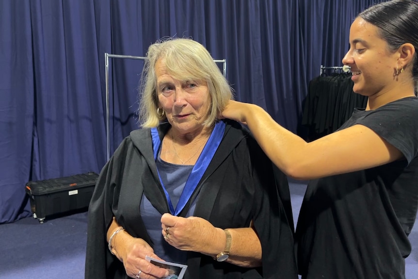 An older woman getting a graduation gown fitted by younger woman.