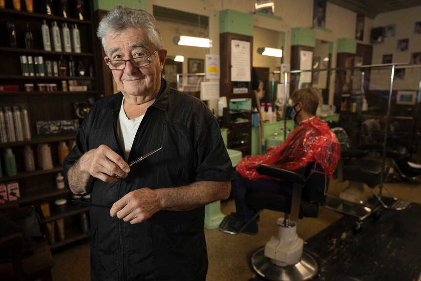 A man in glasses holding a pair of scissors in a barber shop