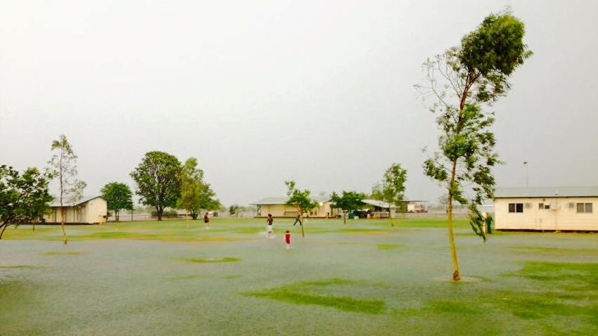 children playing in a flooded lawn in between trees and buildings