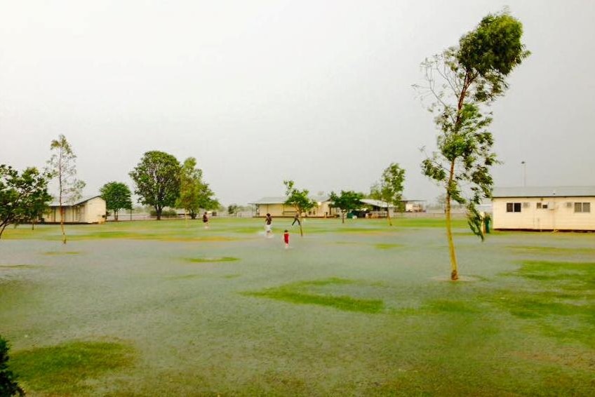 children playing in a flooded lawn in between trees and buildings