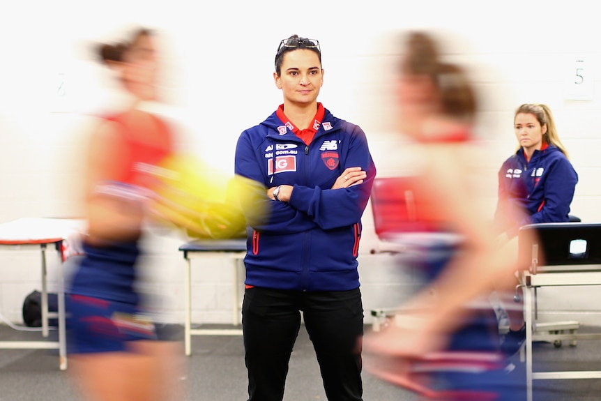 Michelle Cowan folds her arms while in the changeroom as players wizz past in a blur.