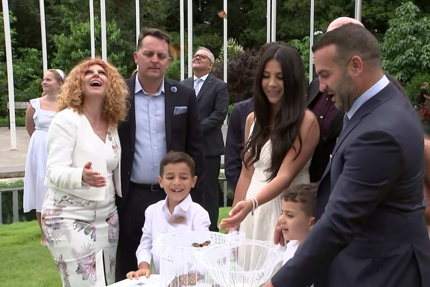 A group of adults and children release butterflies from a white cage.