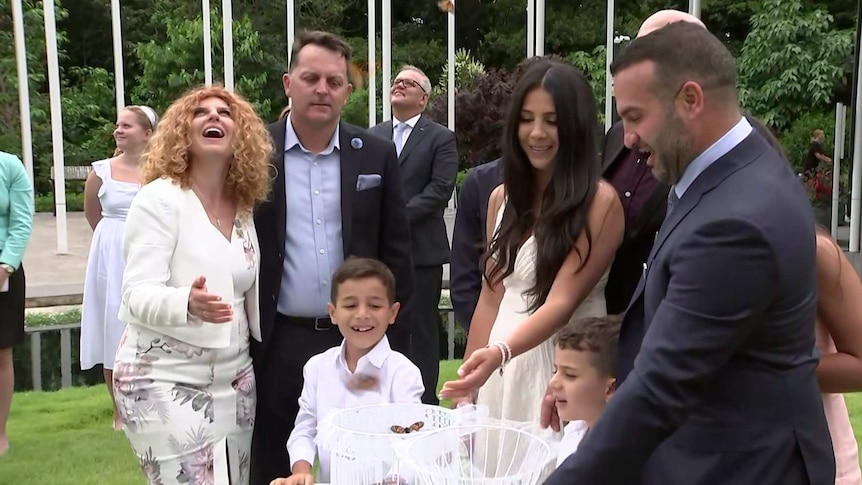 A group of adults and children release butterflies from a white cage.