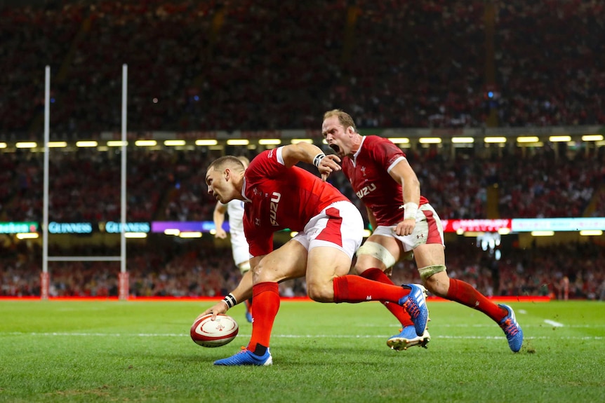 George North puts the ball down one-handed as Alun Wyn Jones screams behind him.