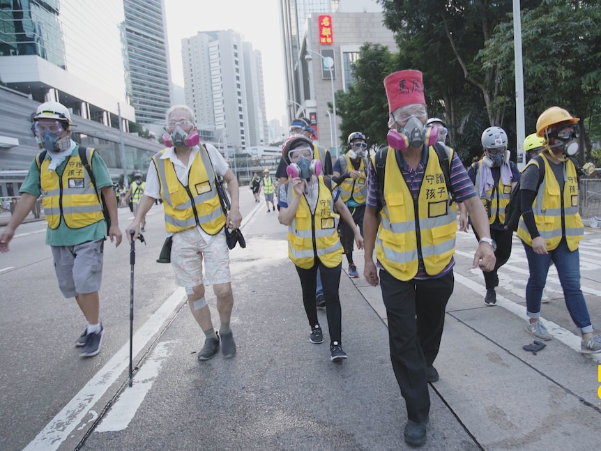 一群穿着黄色夹克、安全帽和防毒面具的老人在街上行走