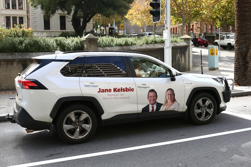 A white SUV on the street with a picture of WA Labor MP Jane Kelsbie and Mark McGowan on its rear driver's side door.