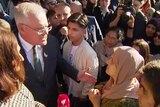 Scott Morrison is surrounded by a tightly packed crowd as he addresses a woman in a hijab.