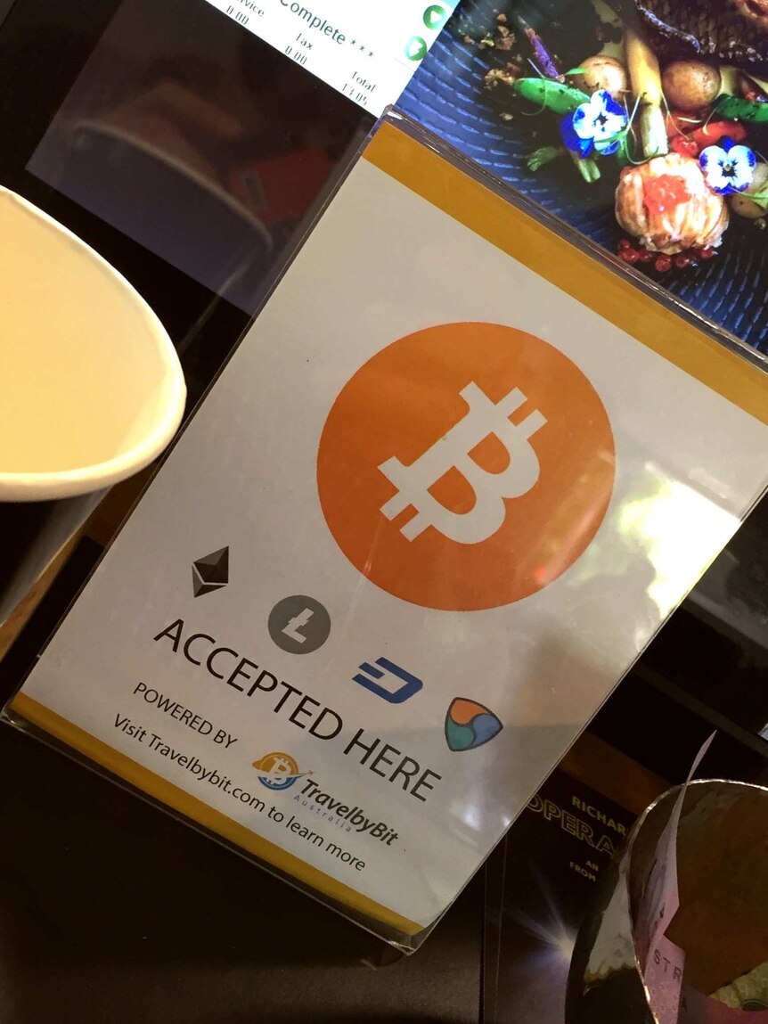 A sign advertising bitcoin is accepted is displayed in front of a cafe cash register.