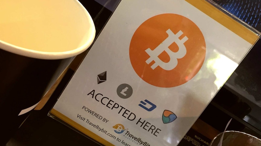 A sign advertising bitcoin is accepted is displayed in front of a cafe cash register.