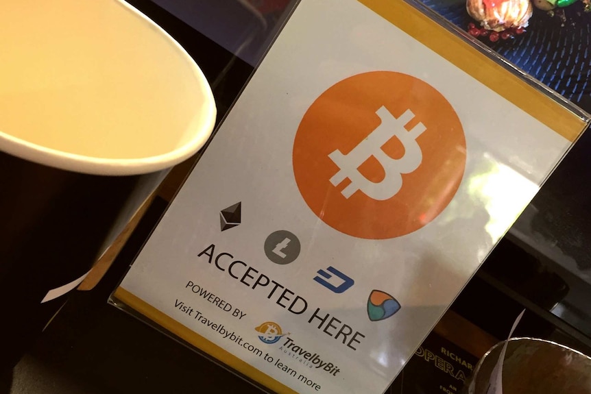 A sign advertising bitcoin is accepted is displayed in front of a cafe cash register.