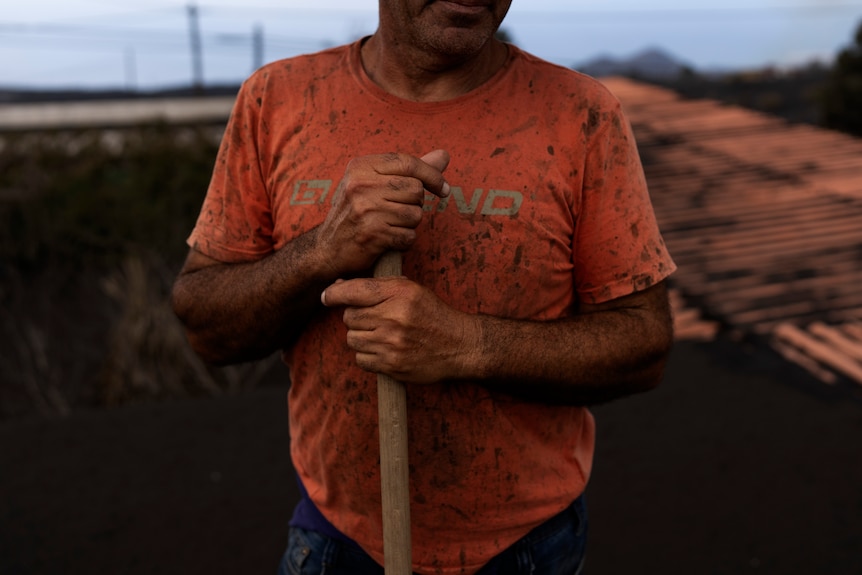Un homme tient un balai alors qu'il nettoie les cendres d'un volcan sur le toit de sa maison.