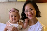 woman holding her baby sitting on a bed.