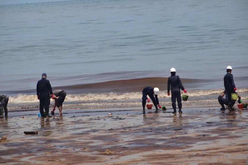 Locals carrying buckets and wearing red gloves cleaning pollution on Balikpapan Bay.