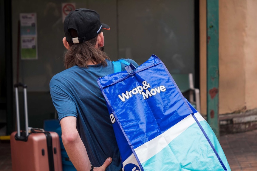 A man carrying a large moving bag wearing a cap.