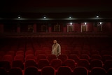 a man stands among red seats in a an empty cinema looking at the camera