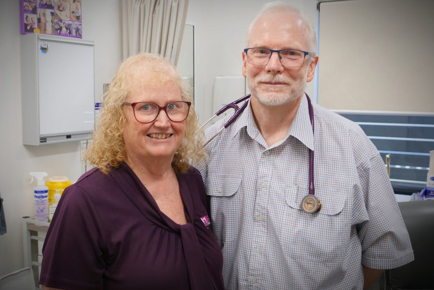 A woman in a purple top with glasses and a man with a stethoscope around his neck standing, smiling at the camera. 
