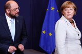 Martin Schulz and Angela Merkel stand in front of a European Union flag.