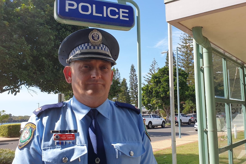 A uniformed police officer standing outside a police station on a sunny day.