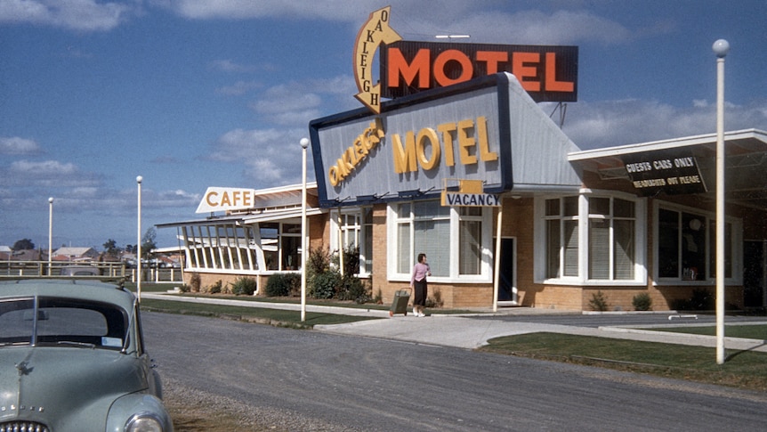 A retro motel in the 50's, large American styles signage decorates the front and an old car is parked out the front