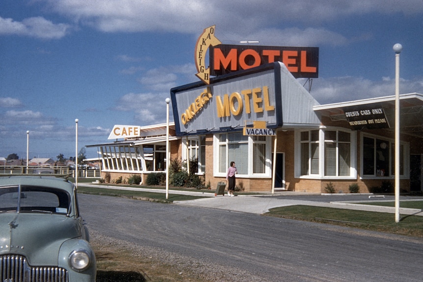 A retro motel in the 50's, large American styles signage decorates the front and an old car is parked out the front