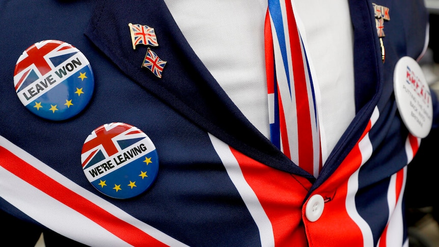 A close-up of a man's blazer in the colours of the union jack, whose lapel is emblazoned with union jack pins.