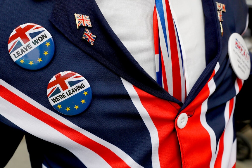 A close-up of a man's blazer in the colours of the union jack, whose lapel is emblazoned with union jack pins.