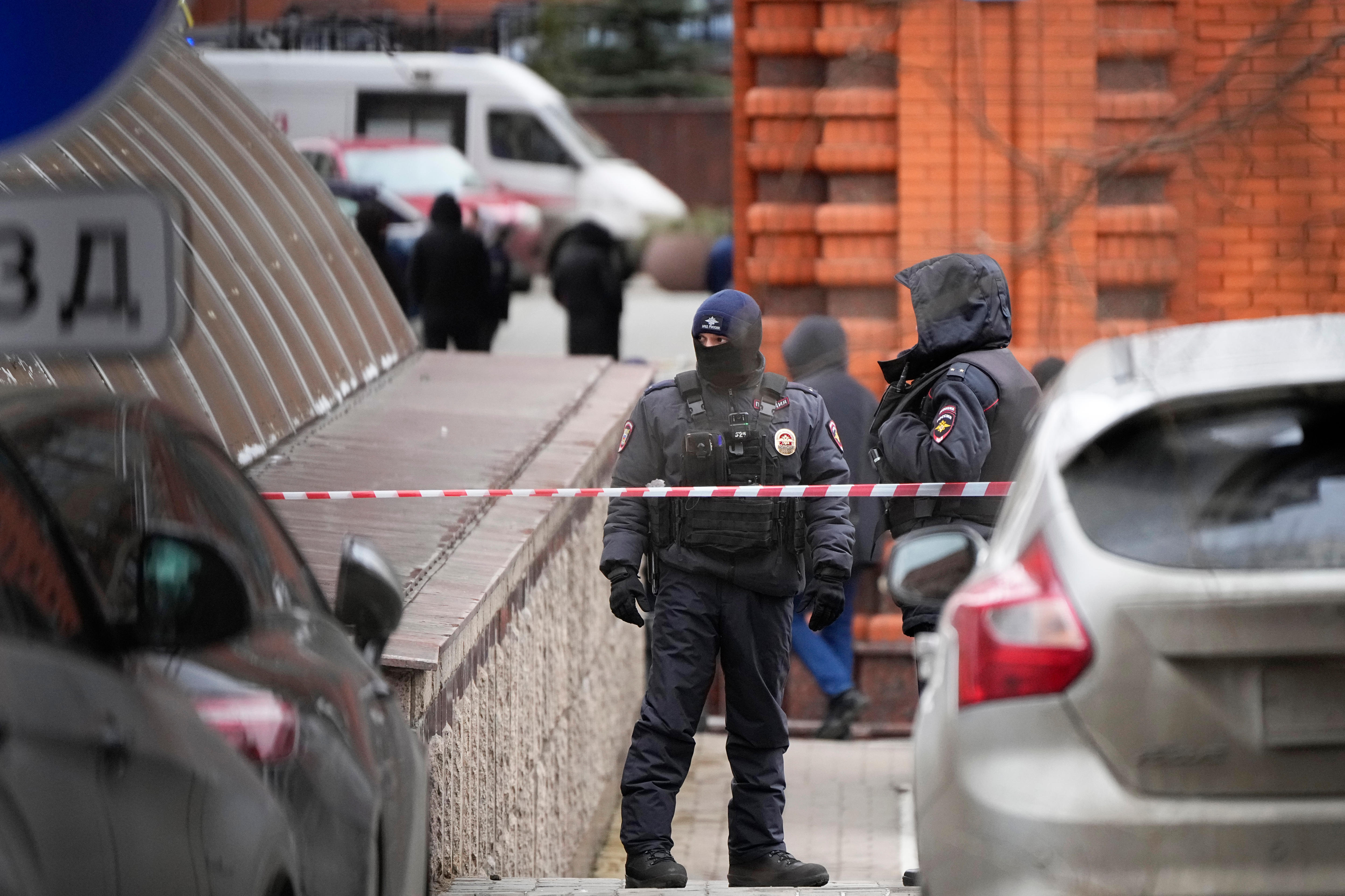 Russian police officers wearing dark protective clothing and standing behind a silver hatchback car and red and white tape line