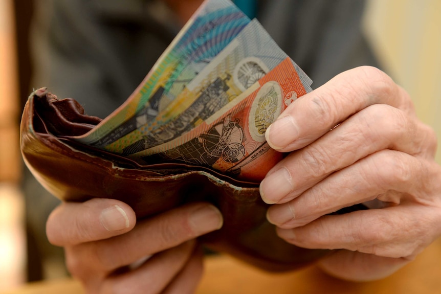 Hands hold Australian banknotes and brown wallet.