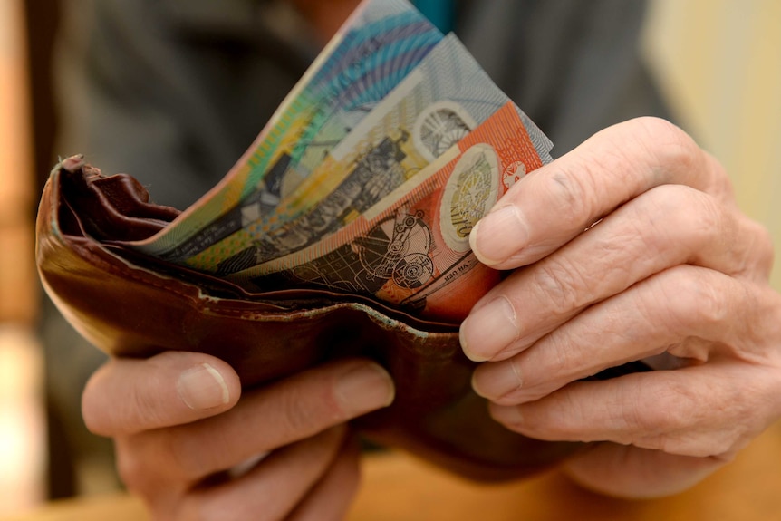 Hands hold onto Australian bank notes and a brown wallet.