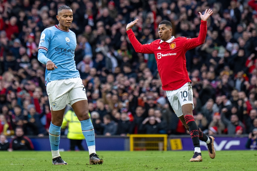 Manchester United's Marcus Rashford puts his hands in the air while a Manchester City player looks sad.