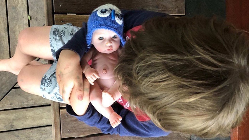 Little boy sitting down and holding his realistic baby doll