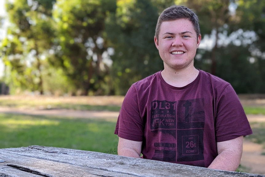 A young boy in a tshirt sits and smiles  