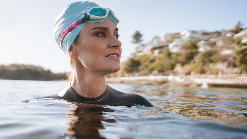 Julia Baird, who is wearing a blue swim cap and goggles submerged in the sea, looks back at the shore in warm morning sunlight