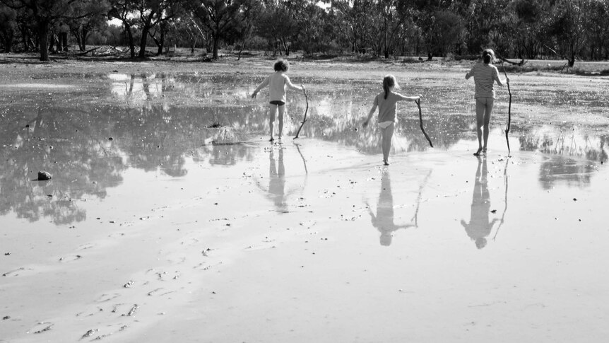 Kids walk with sticks in the mud.