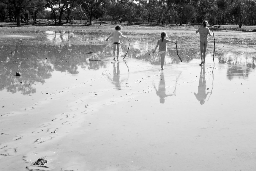 Kids walk with sticks in the mud.