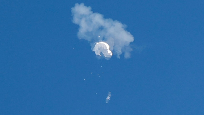 A plume of smoke and debris surrounds a white balloon as it falls from the sky.