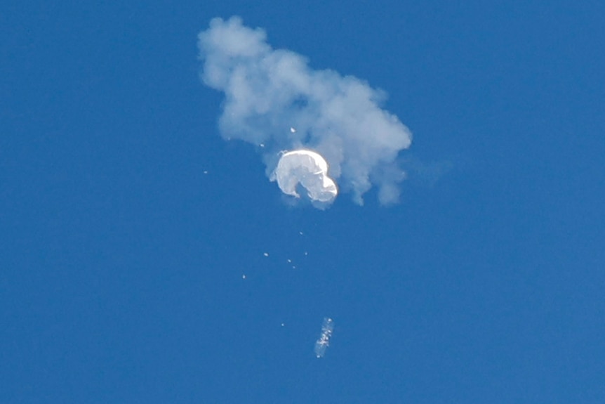 A plume of smoke and debris surrounds a white balloon as it falls from the sky.