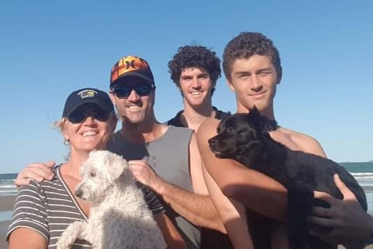 The Yore family, Mandy, Shane, Mitchell and Rhys, stand together holding two dogs on a beach.