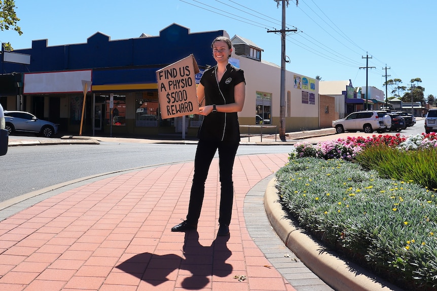 A Goldfields Physio employee stands at a round about with a sign advertising a $5,000 reward