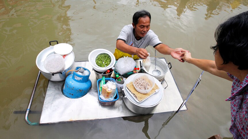 A food vendor gives change to a customer along a flooded street in the Thai town of Sena