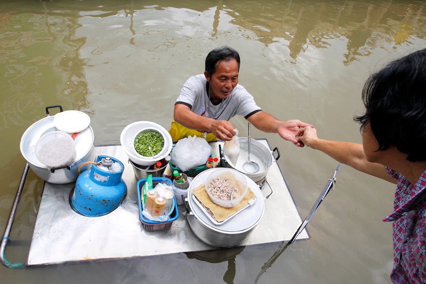 A food vendor gives change to a customer along a flooded street in the Thai town of Sena